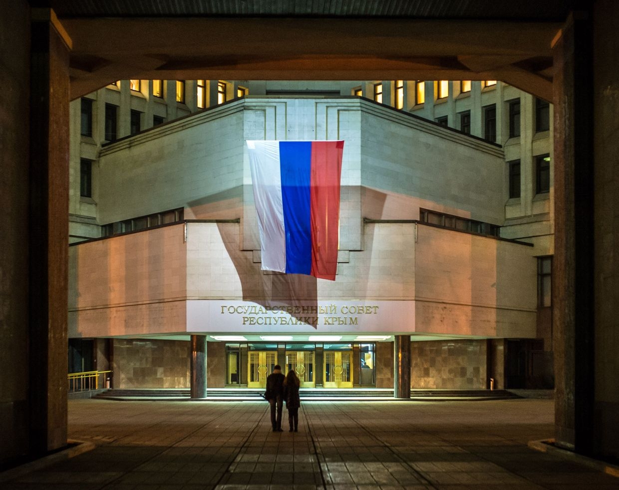 People walk outside the building of the Crimean parliament, bearing a Russian flag in occupied Simferopol, Ukraine on March 20, 2014.