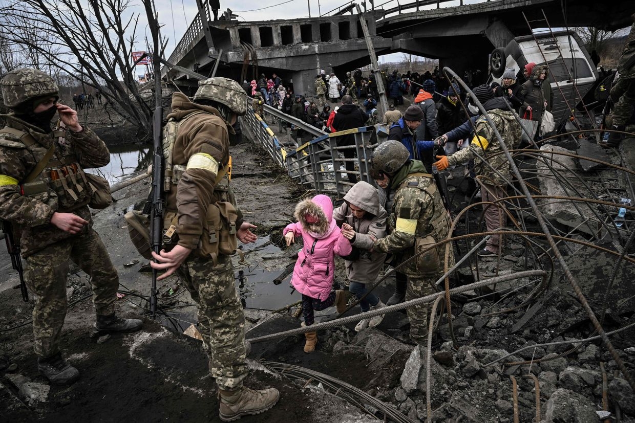 People cross a destroyed bridge as they evacuate the city of Irpin, northwest of Kyiv, during heavy shelling and bombing