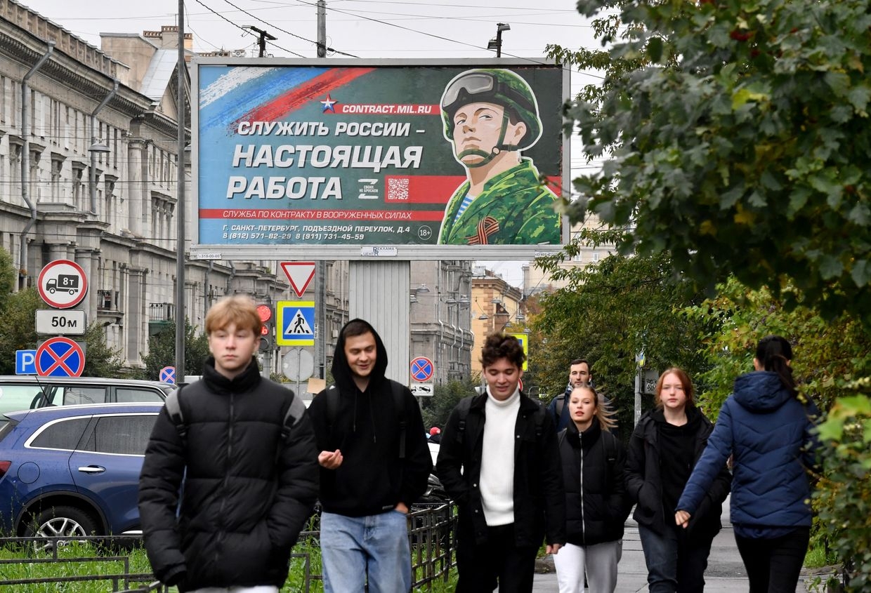 Youths walk past a billboard promoting contract army service with an image of a serviceman and the slogan “Serving Russia is a real job” in Saint Petersburg, Russia, on Sept. 29, 2022. 
