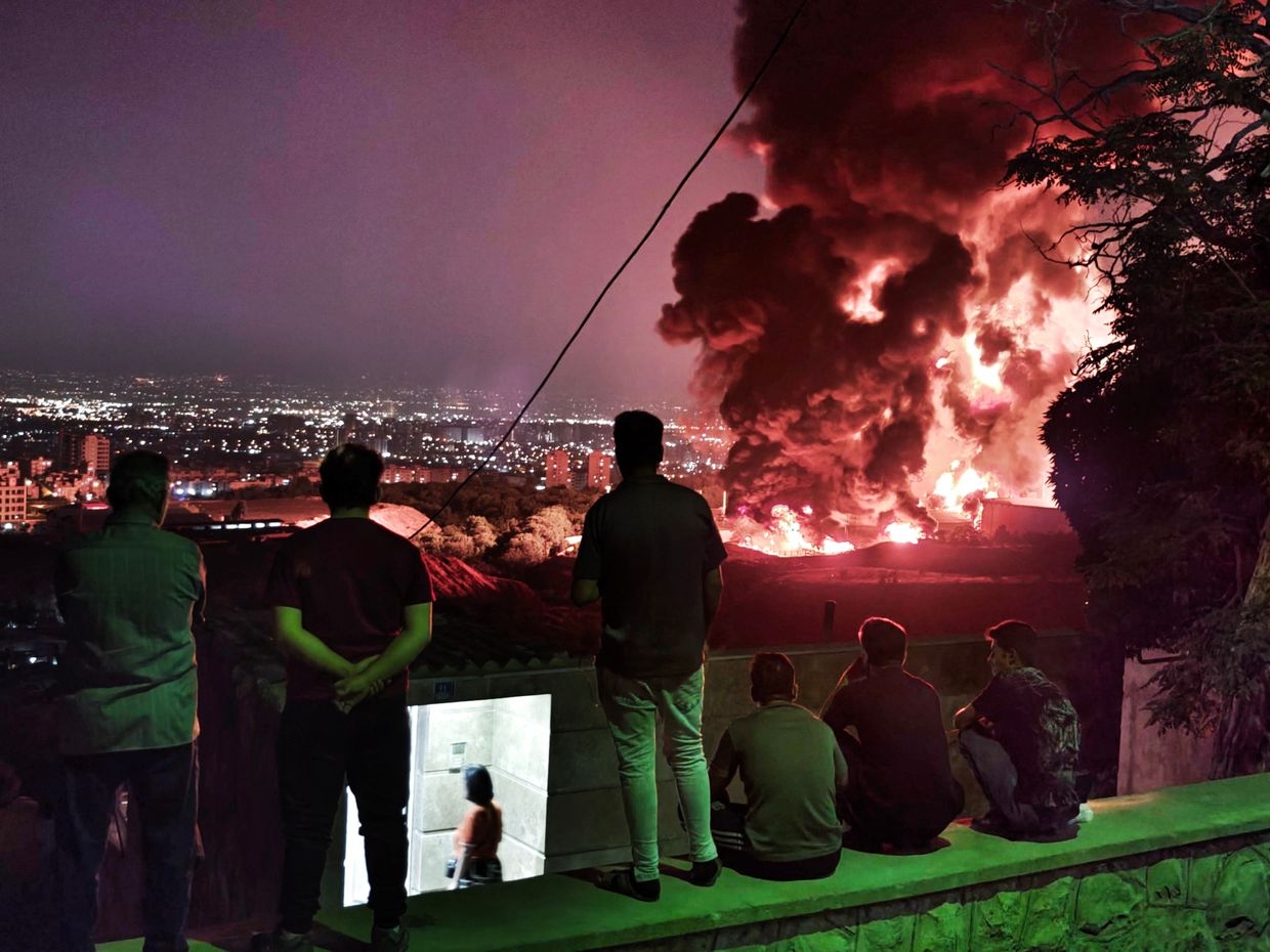 People observe fire and smoke from an Israeli attack on the Shahran oil depot in Tehran, Iran, on June 15, 2025.