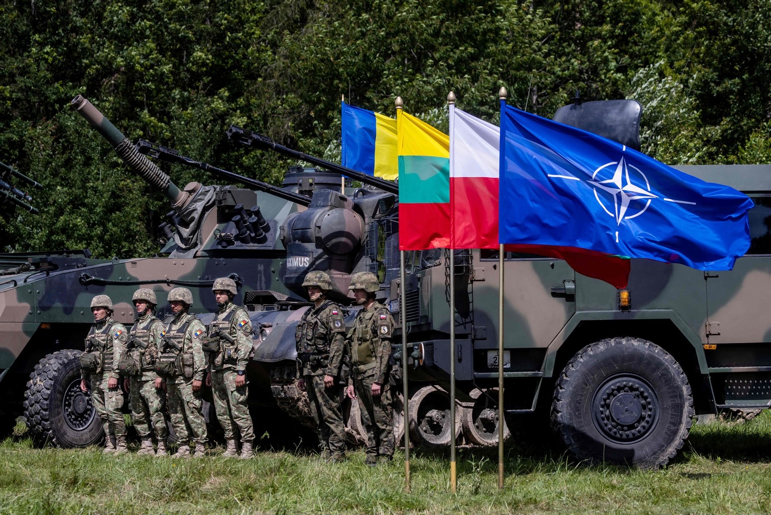 Polish and Romanian soldiers stand by NATO vehicles in Szypliszki village, in north-eastern Poland, on July 7, 2022. 