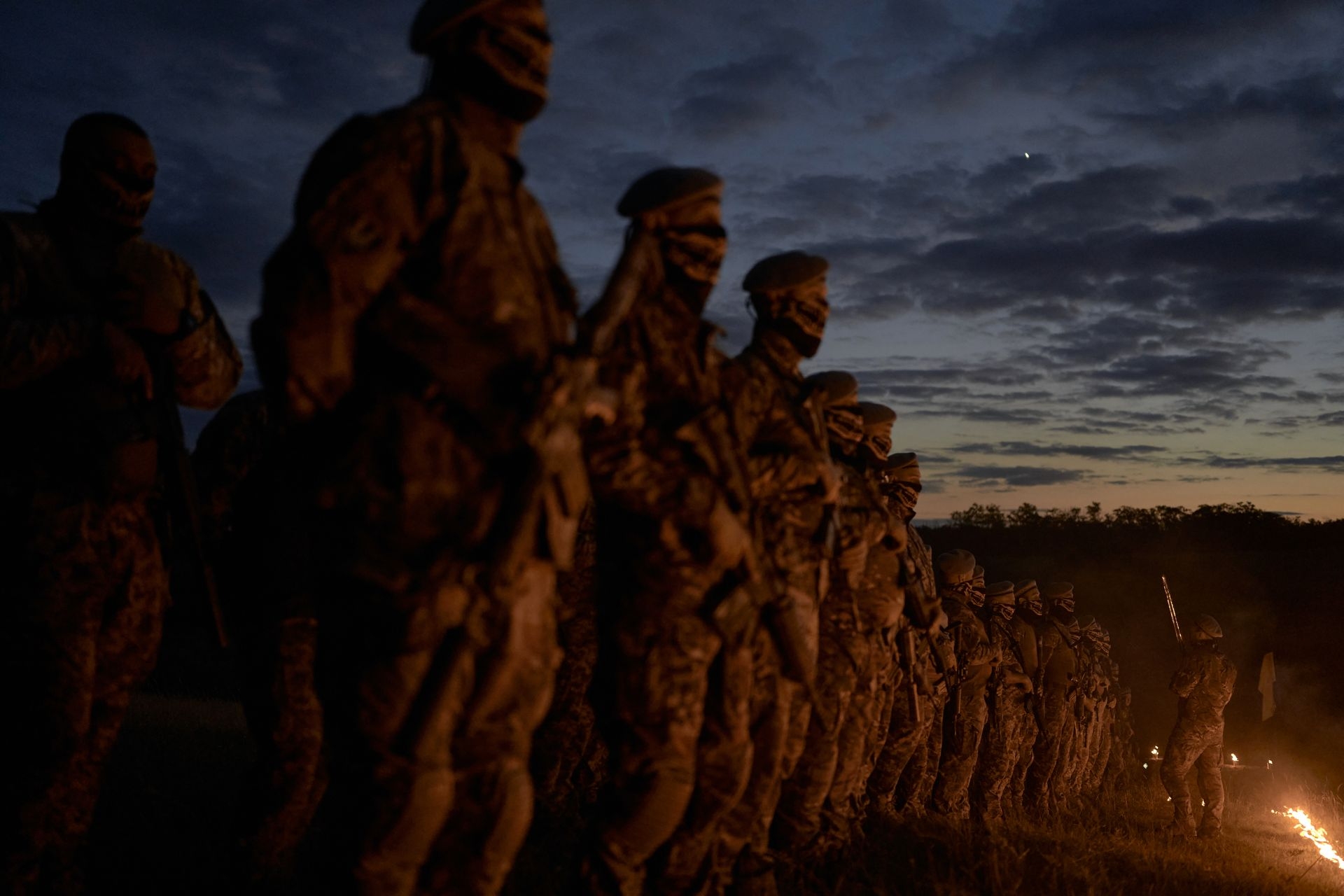 A squad commander initiates fighters into the unit with a sword during a torchlit ceremony in an unspecified location in Ukraine on June 29, 2025. 