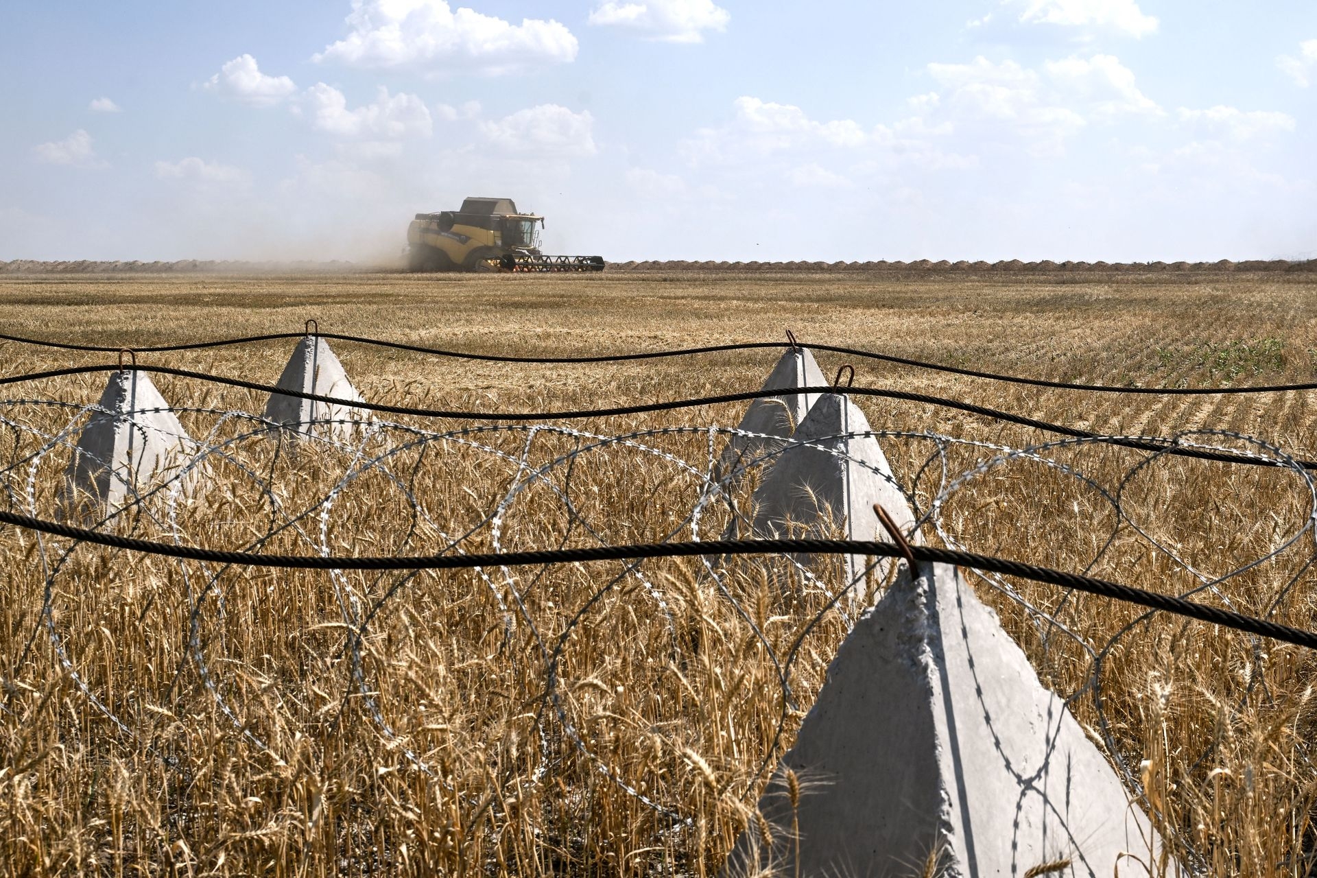 A combine harvester collects grain near anti-tank obstacles and barbed wire in a field outside Orikhiv, Zaporizhzhia Oblast, Ukraine, on July 8, 2025. 