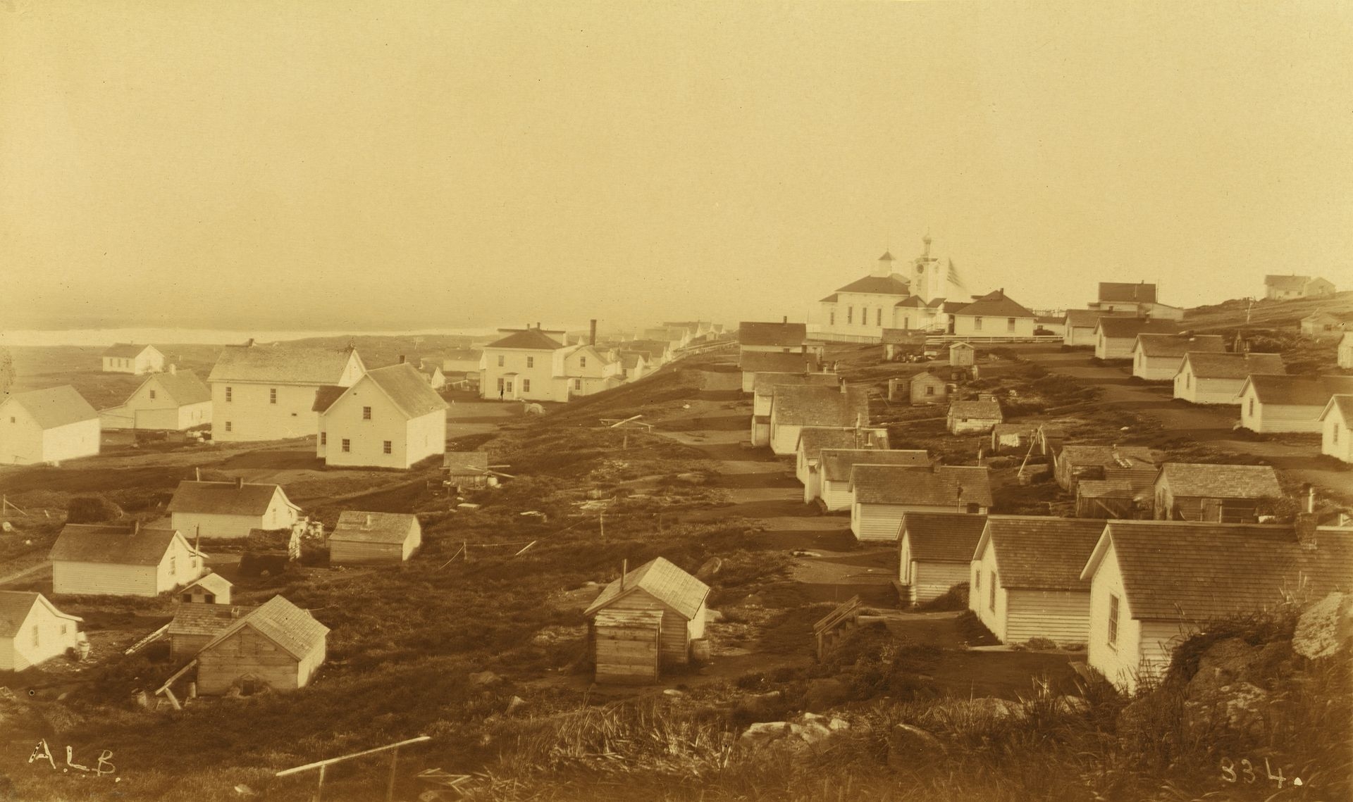 An unidentified village, possibly on Unalaska Island, U.S., with a Russian church featuring a clock in the bell tower in the background, in 1894 or 1895.
