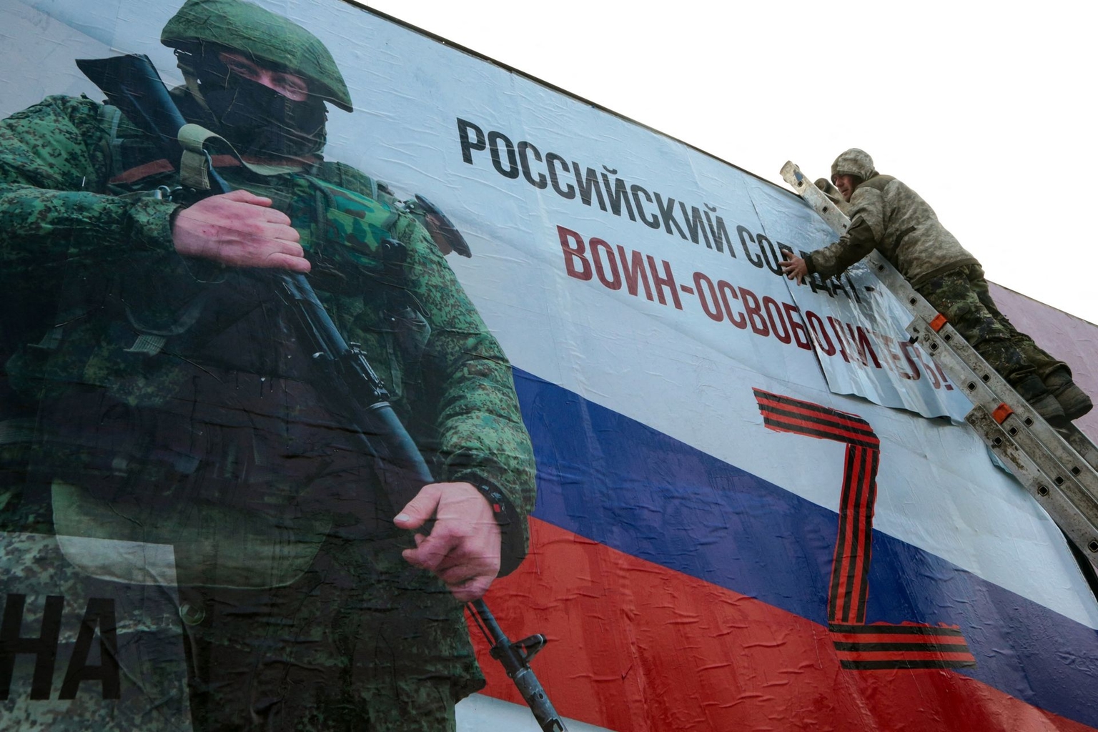 A man finishes gluing a large Russian propagandist placard depicting a Russian soldier with the caption “A Russian soldier is a liberator!” in the city center of Simferopol, Crimea, Ukraine, on March 4, 2022.