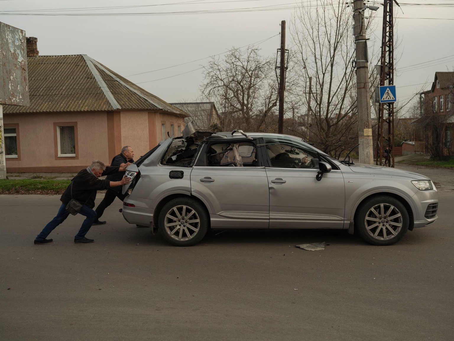 Kherson residents attempt to put a car into neutral and move it off the road after it was struck by an FPV drone in Kherson, Ukraine, on Nov. 23, 2025.