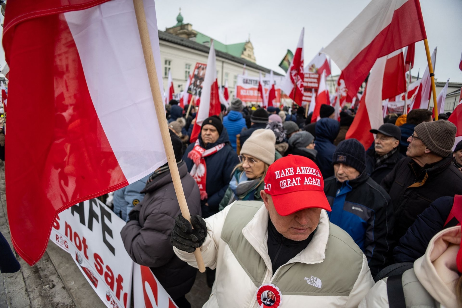 A man wearing a "Make America Great Again" hat holds a Polish flag during a demonstration against the European Union's SAFE (Security Action for Europe) program in front of the Presidential Palace in Warsaw, Poland, on Feb. 21, 2026.