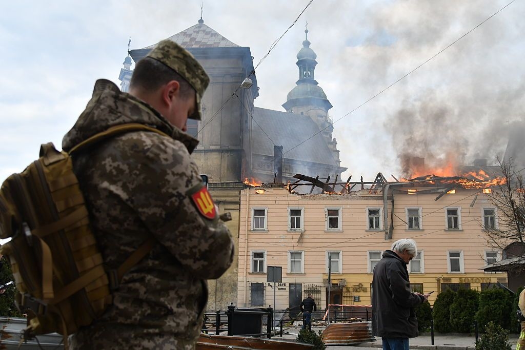 A man in military uniform stands in front of a burning building in central Lviv, Ukraine, following a Russian drone strike on March 24, 2026. 