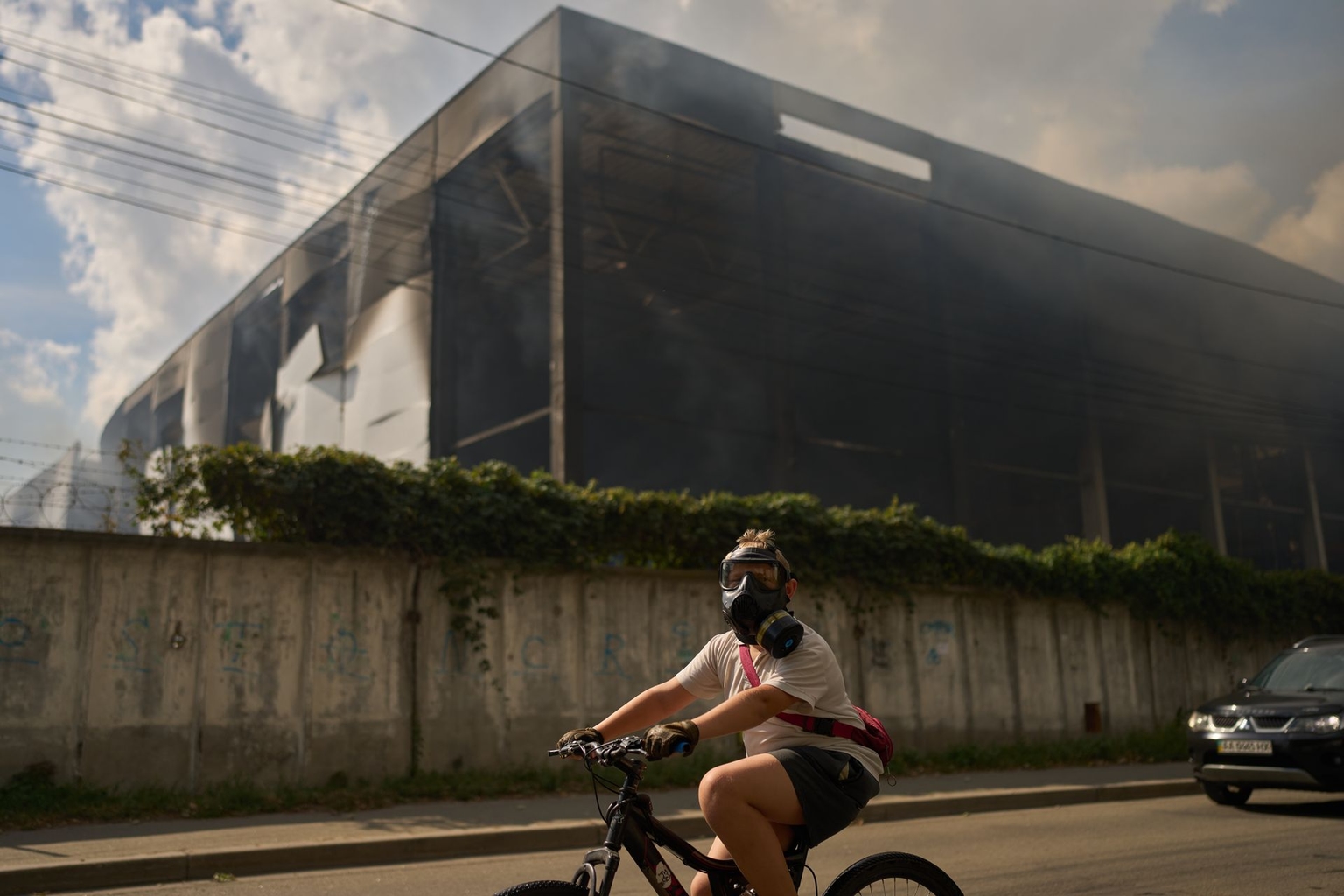 A person wears a protective mask as they ride a bicycle past a partially destroyed warehouse after a Russian drone attack in Brovary, on the outskirts of Kyiv, Ukraine, on Sept. 4, 2026.
