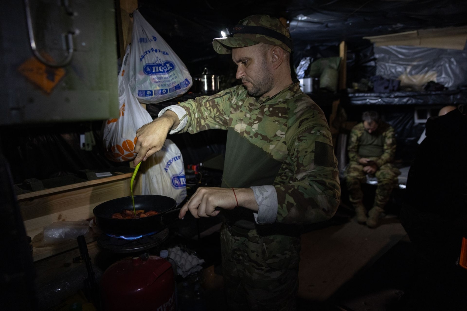 Kalash, a combat wing operator of the Darts crew of the NAFO, cooks breakfast on a camping stove in the dugout, Lyman sector, Ukraine, on Aug. 11, 2026. 
