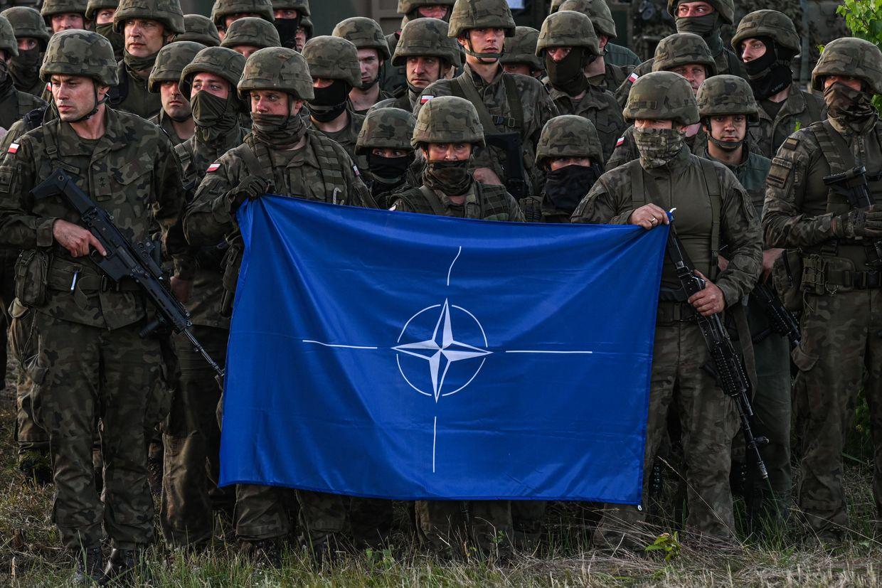Soldiers hold a NATO flag during a training demo with the NATO battle group at Orzysz training ground, Poland, Jul. 3, 2022.