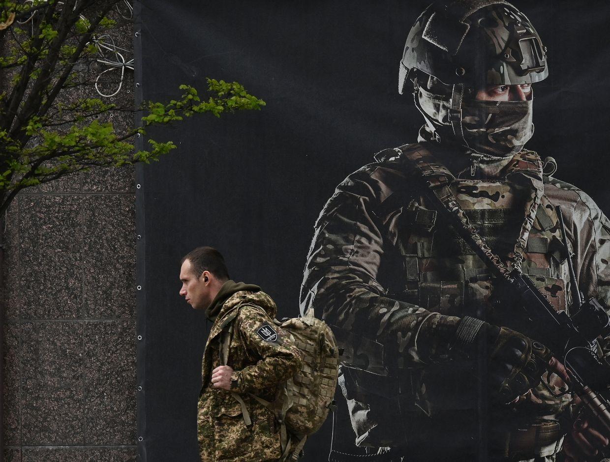  A Ukrainian serviceman passes a recruiting poster in Kyiv, Ukraine, on April 23, 2024