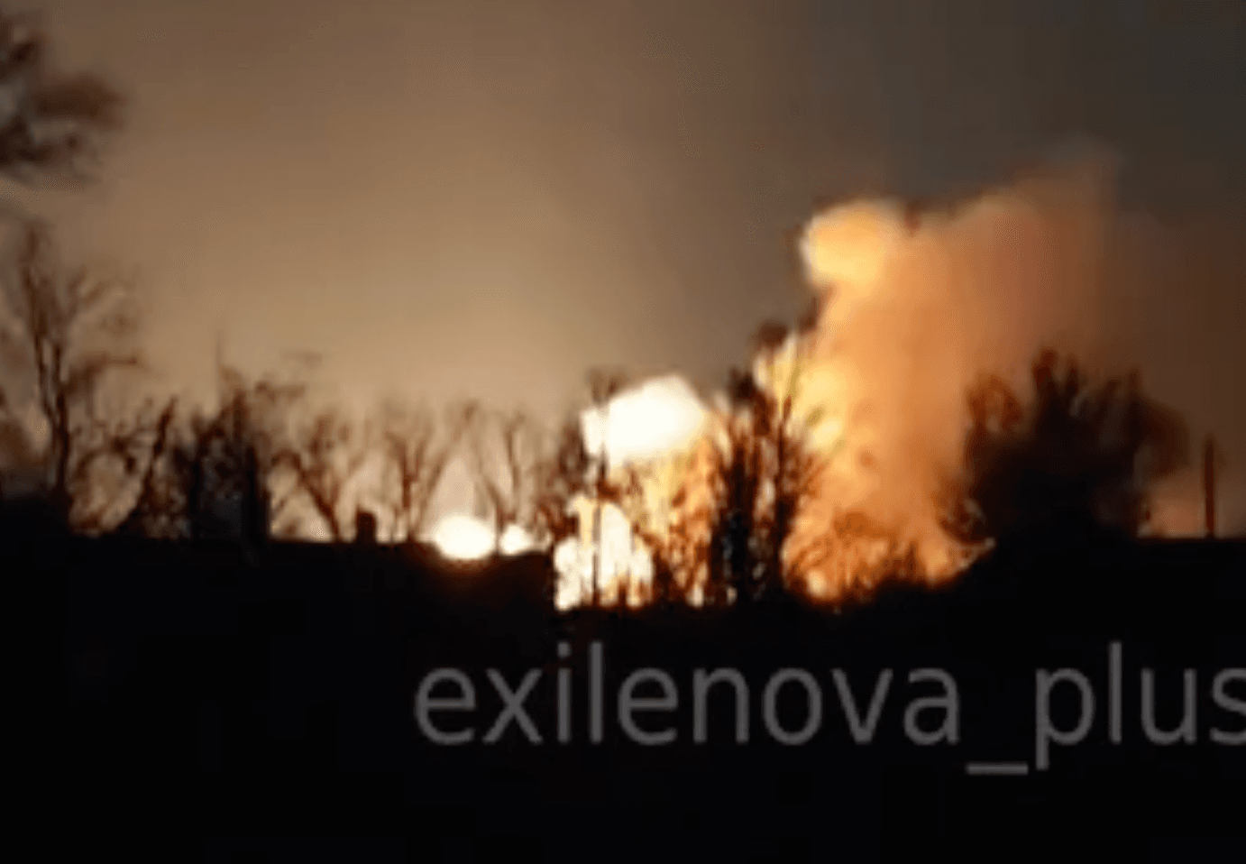 A large explosion erupts in the distance behind a dark treeline