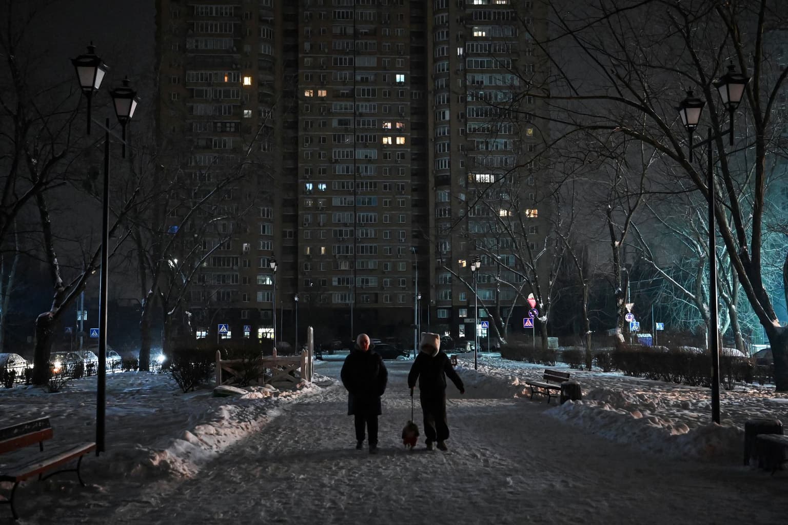 People walk with a dog along an unlit, snow-covered street during a power outage in Kyiv, Ukraine, on Jan. 13, 2026. 