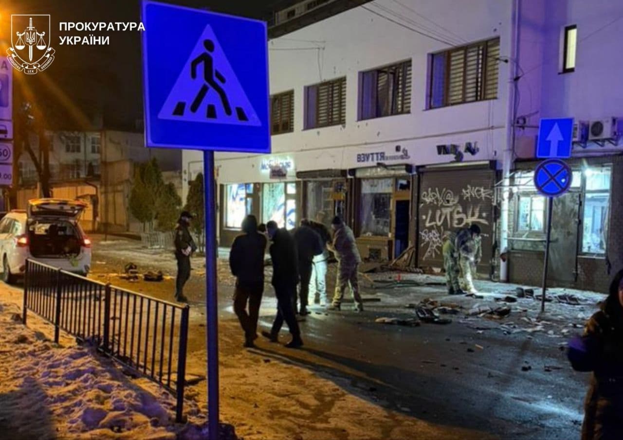 Small shops with shattered windows line a street covered in rubble