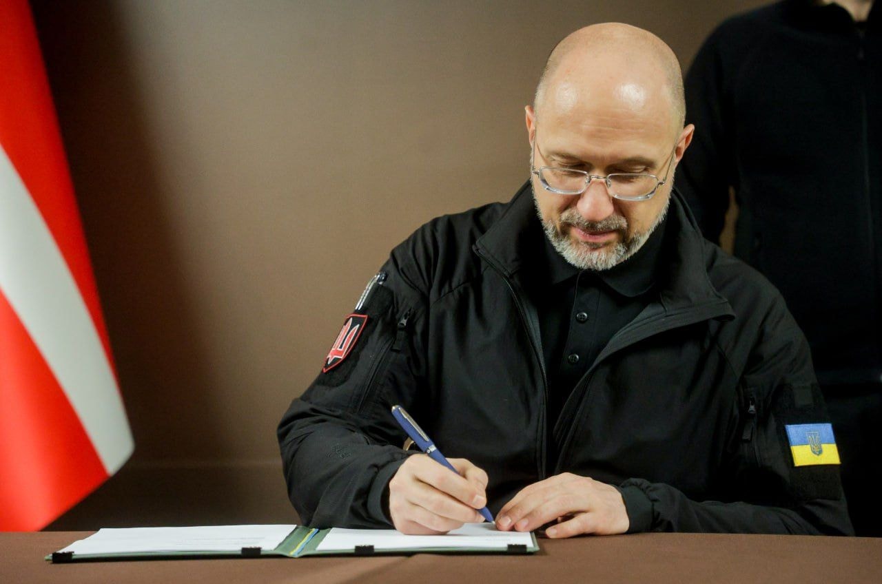 Sitting by a Danish flag, Defense Minister Denys Shmyhal signs a document.