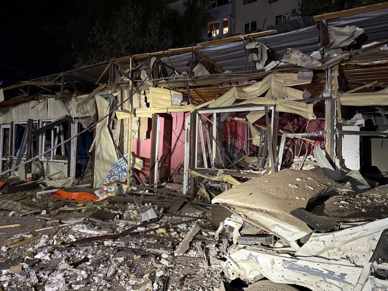 Damaged shops infront of a residential building under a night sky.