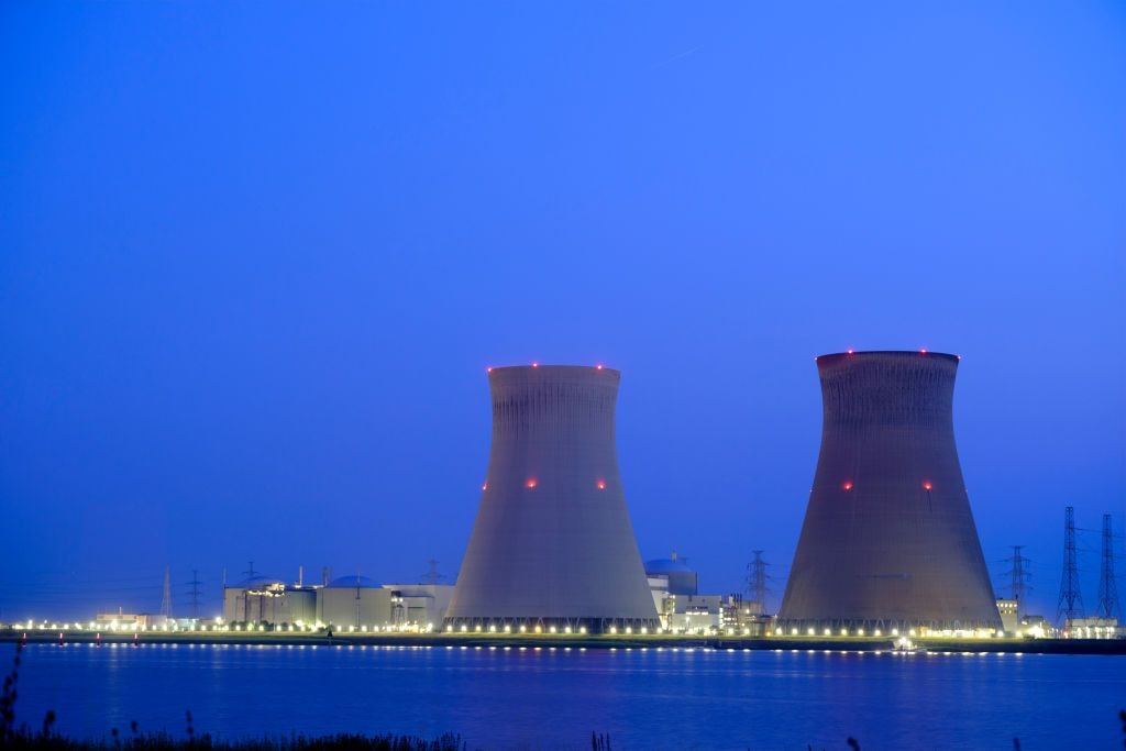 Two nuclear reactors along a water body under a dark blue sky