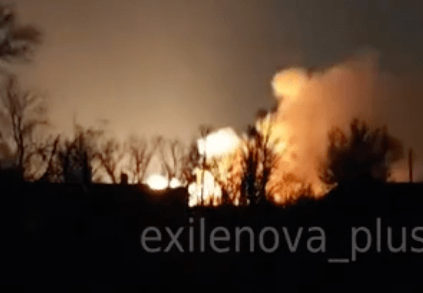 A large explosion erupts in the distance behind a dark treeline