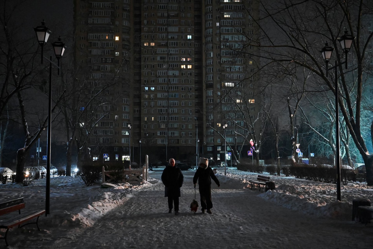 People walk with a dog along an unlit, snow-covered street during a power outage in Kyiv, Ukraine, on Jan. 13, 2026. 