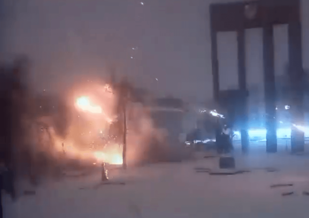 A blast erupts over a snowy city-square under a dusky sky