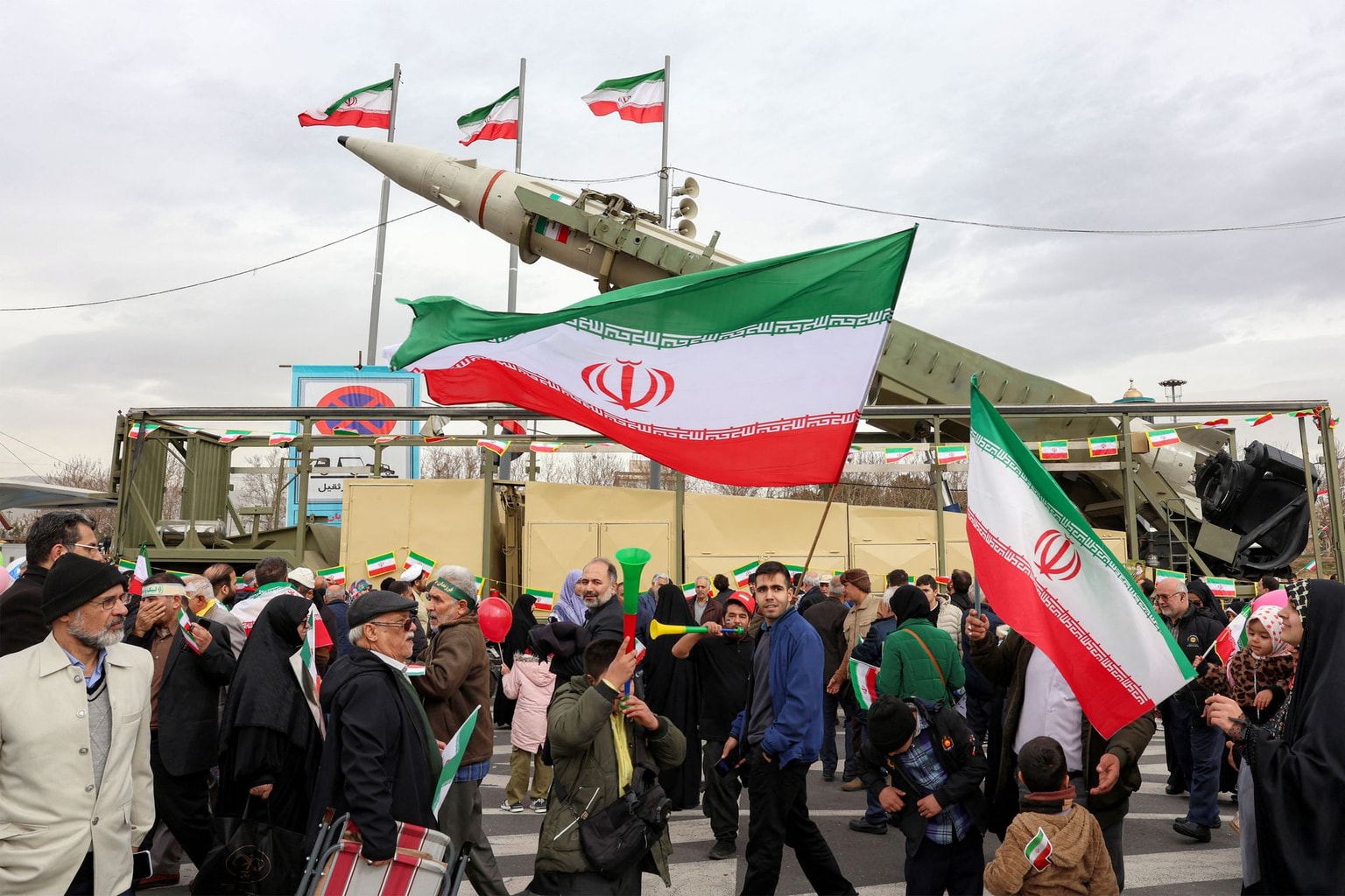 People walk with Iranian national flags near a ballistic missile launch vehicle in Tehran, Iran, on Feb. 11, 2026