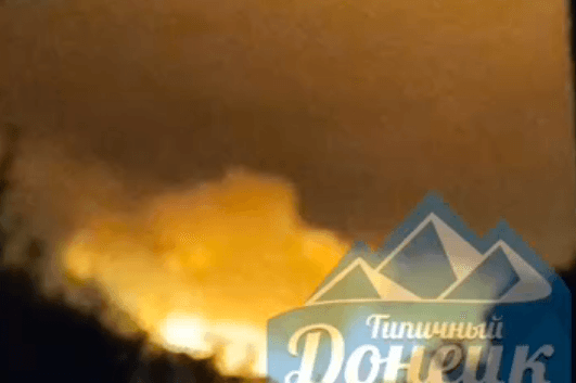 A large explosion occurs in the distance under a dark sky.