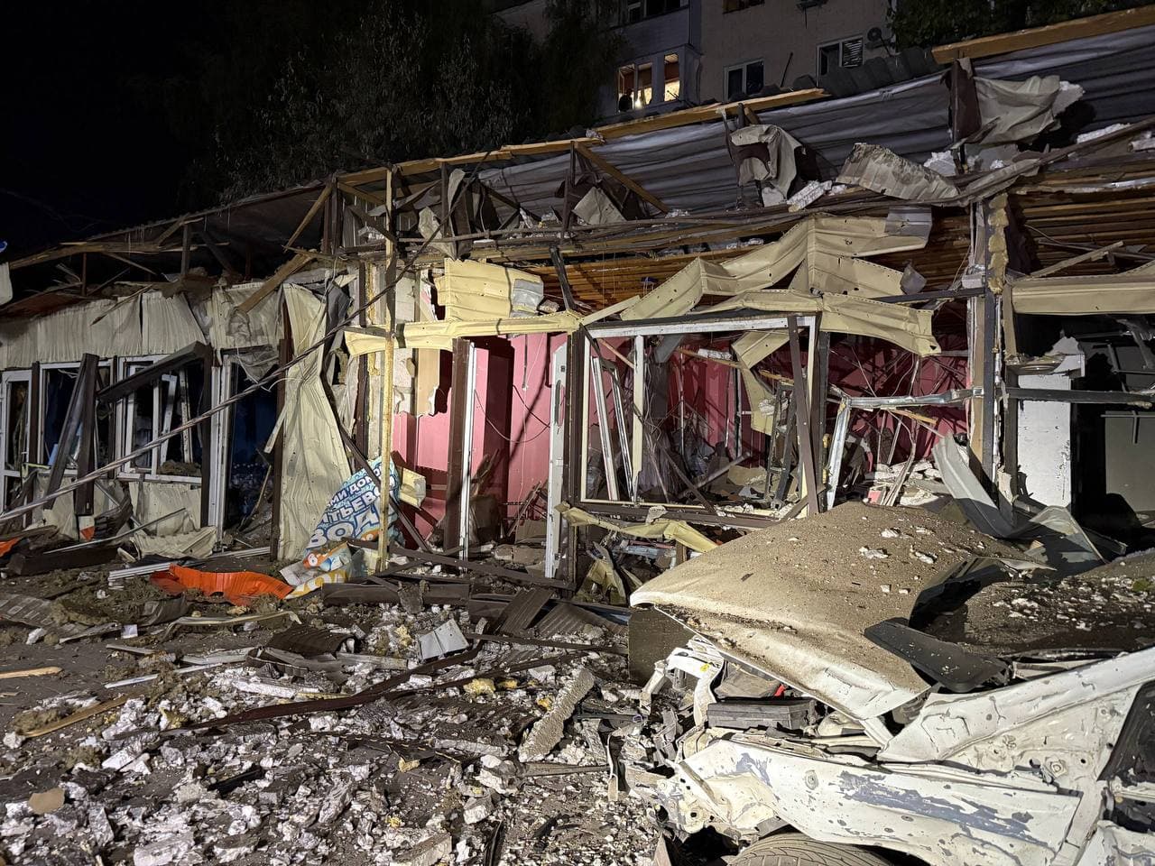 Damaged shops infront of a residential building under a night sky.
