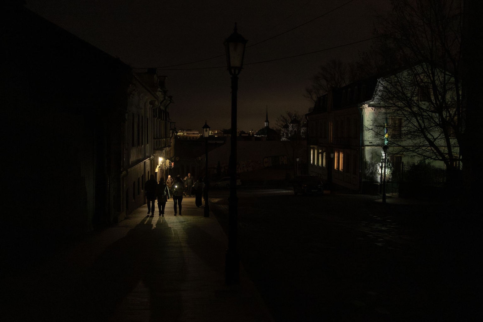 People walk along a darkened street during a partial blackout in the Podil neighborhood of Kyiv, Ukraine, on Nov. 25, 2025.
