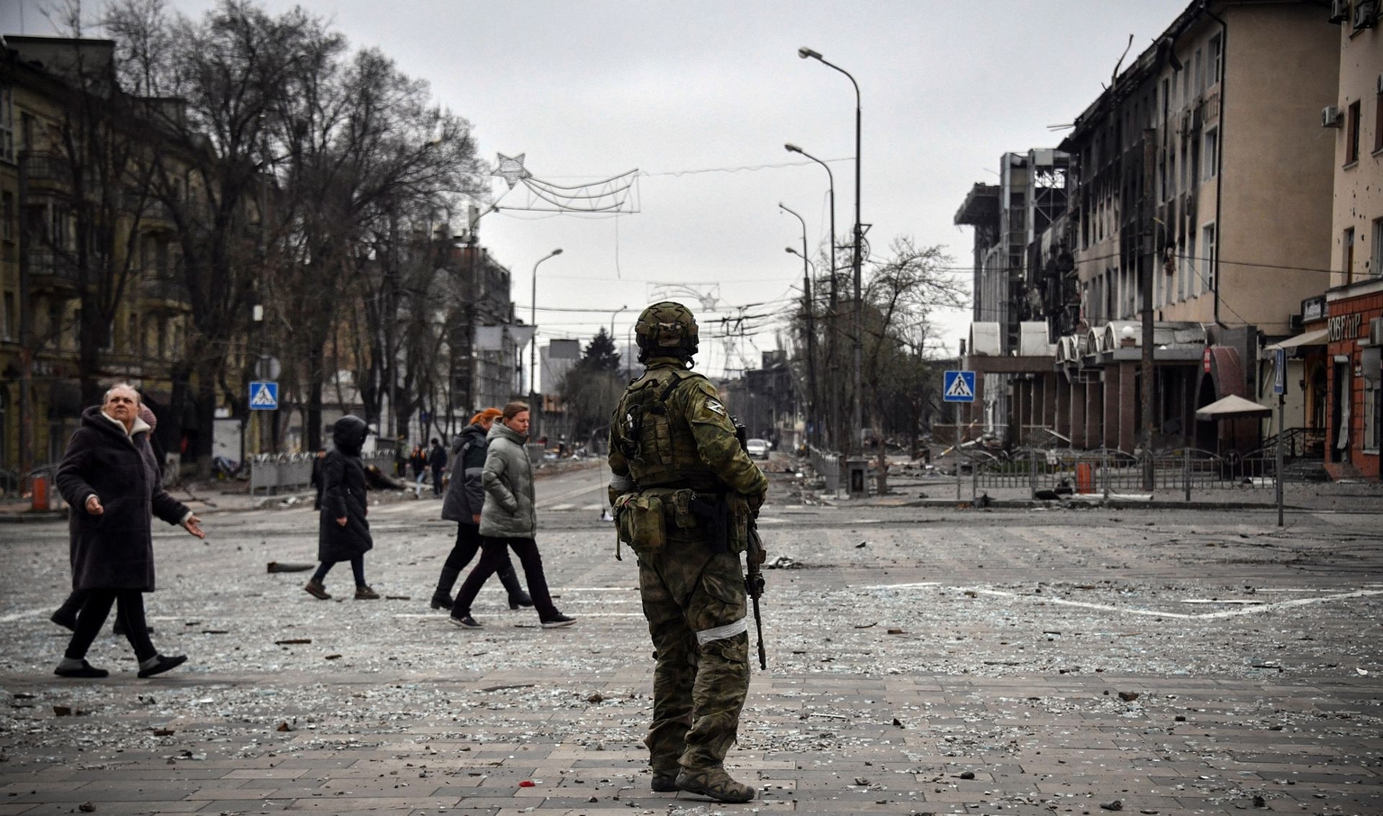 People pass by a Russian soldier in central Mariupol, Ukraine, on April 12, 2022