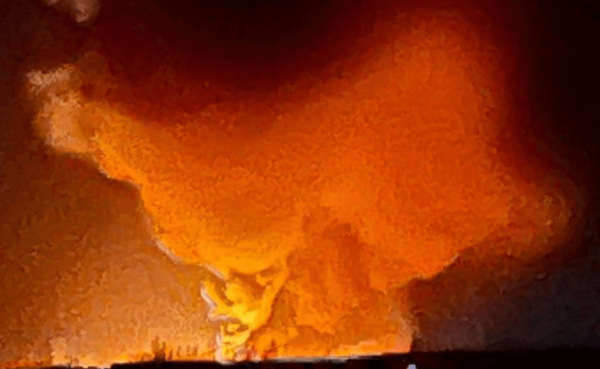 A large explosion erupts in the distance under a dark sky.