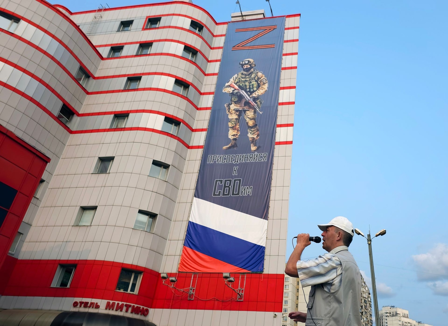 A street musician sings a song beneath a military billboard seeking conscripts for the armed forces, installed on the wall of a building in Moscow, Russia, on June 10, 2025.