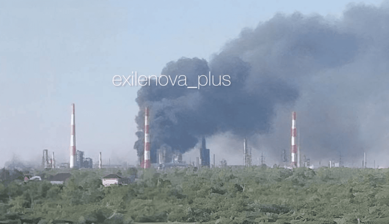 Dark smoke rises from an oil refinery with red and white striped smokestacks