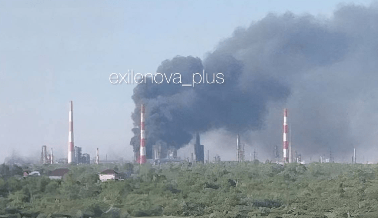 Dark smoke rises from an oil refinery with red and white striped smokestacks