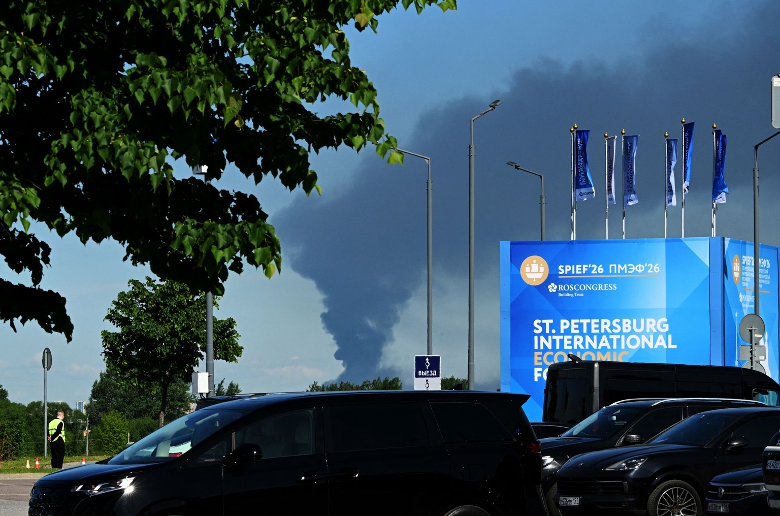 Cars are parked near banners for the St. Petersburg International Economic Forum as black smoke rises in the distance in St. Petersburg, Russia, on June 3, 2026