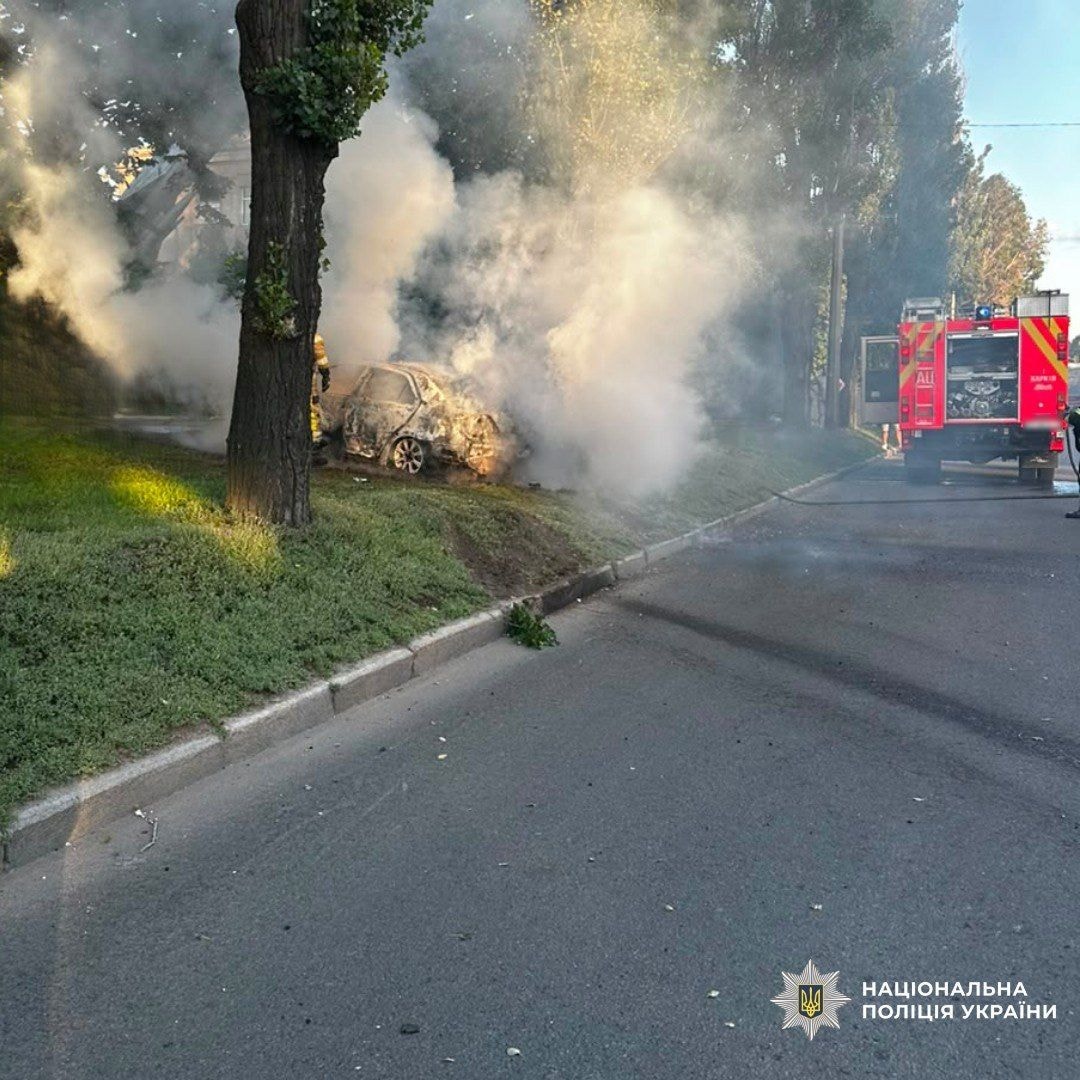 Firefighters extinguish a burning car on the side of a road
