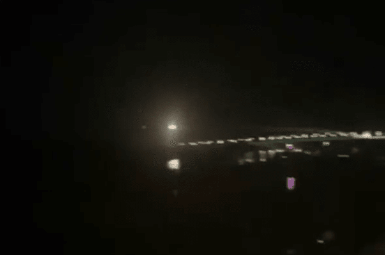 A bright spark flies over a cityscape under a night sky