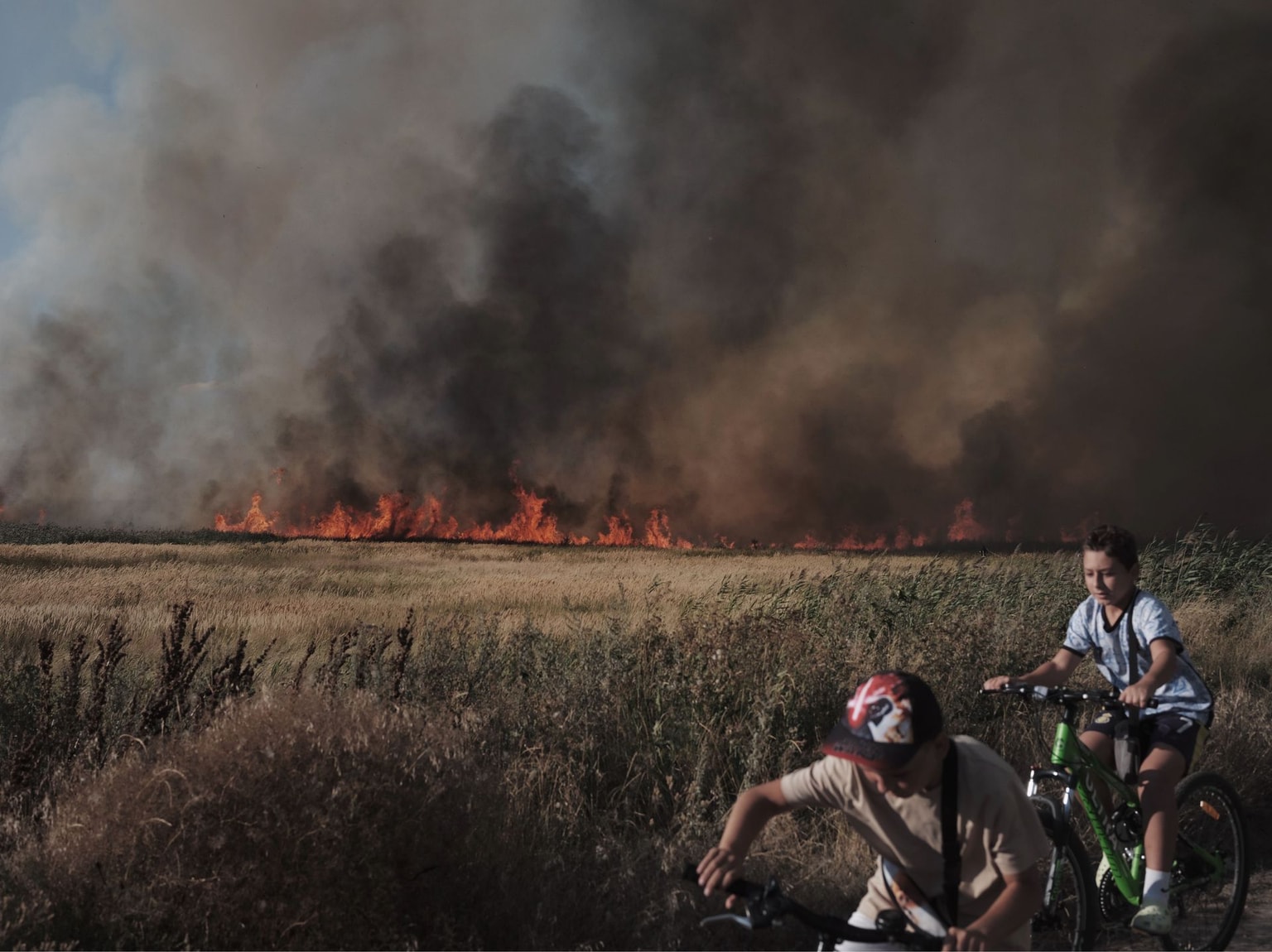 Children on bicycles watch a fire near their home in Pavlohrad, Ukraine, on August 15, 2026.