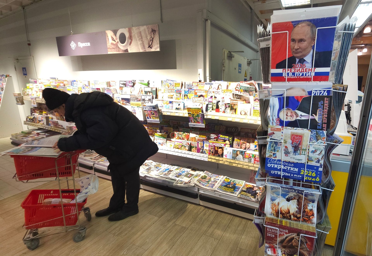 A shopper reads a newspaper next to Putin calendars at an Auchan store in Moscow, Russia, on December 6, 2025.