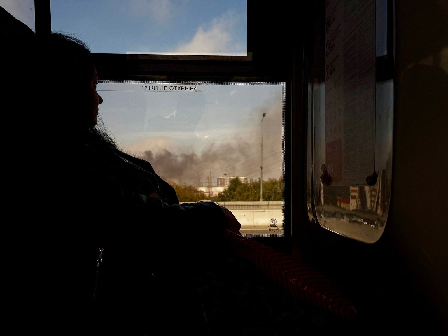 A woman rides on a bus as smoke rises near oil refinery in Moscow, Russia, on Sept. 20, 2026.